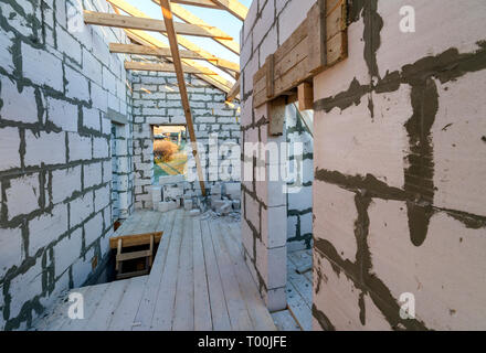 House interior under construction and renovation. Energy saving walls of hollow foam insulation blocks and bricks, ceiling beams and roof frame. Stock Photo