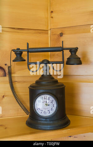 Black decorative metal antique telephone with integrated clock face on pinewood shelf in basement inside piece sur piece Eastern white pine log home Stock Photo