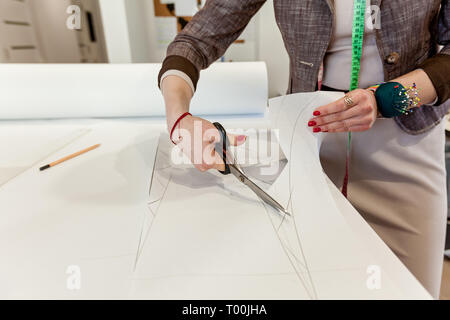 Women's hands cut the pattern out of paper with tailors' scissors on a white table Stock Photo
