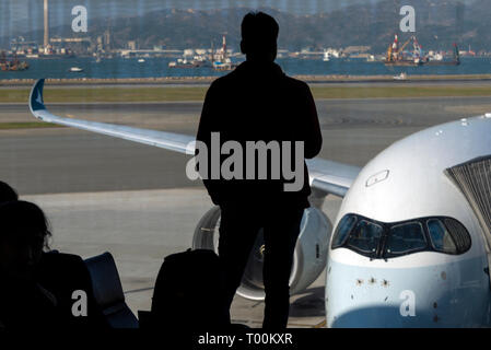 Silhouette of a passenger at the boarding gate window, awaiting to board an Airbus A350 airliner, Hong Kong Airport. Stock Photo