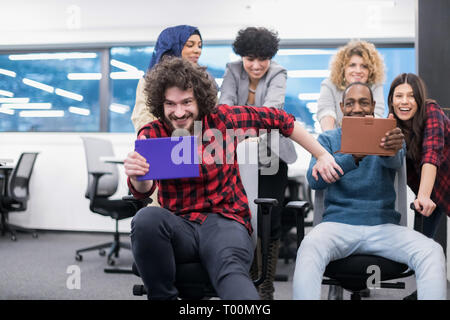 multiethnics startup business team of software developers having fun while racing on office chairs,excited diverse employees laughing enjoying funny a Stock Photo