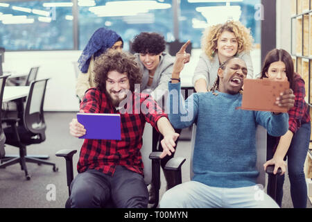 multiethnics startup business team of software developers having fun while racing on office chairs,excited diverse employees laughing enjoying funny a Stock Photo