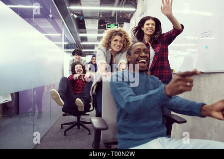 multiethnics startup business team of software developers having fun while racing on office chairs,excited diverse employees laughing enjoying funny a Stock Photo