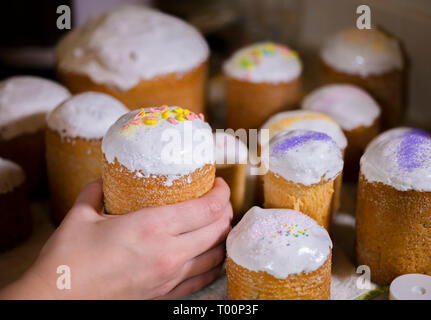 Baker decorates the upper part of Easter cakes covered with white sugar icing by colored granulated sugar pouring decoration on fresh icing making tra Stock Photo