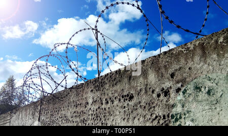 Barbed wire on a dark fence. Against a blue sky with clouds Stock Photo