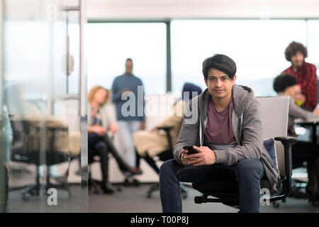 young indian male software developer using mobile phone writing messages while having break at modern creative startup office Stock Photo