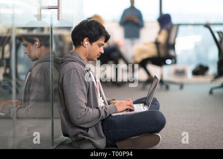 young indian software developer man using laptop computer writing programming code while sitting on the floor at modern creative startup office Stock Photo