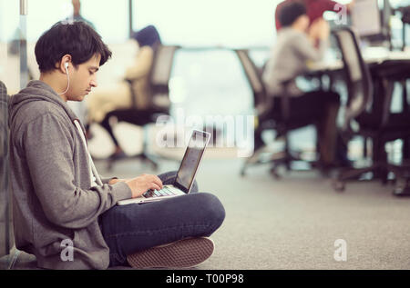 young indian software developer man using laptop computer writing programming code while sitting on the floor at modern creative startup office Stock Photo