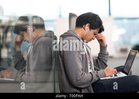 young indian software developer man using laptop computer writing programming code while sitting on the floor at modern creative startup office Stock Photo