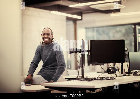 Portrait of young smiling african american male software developer sitting on office desk at modern startup office Stock Photo