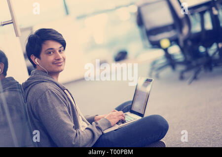 young indian software developer man using laptop computer writing programming code while sitting on the floor at modern creative startup office Stock Photo