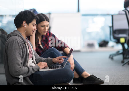 young software developers couple using laptop computer writing programming code while sitting on the floor at modern creative startup office Stock Photo