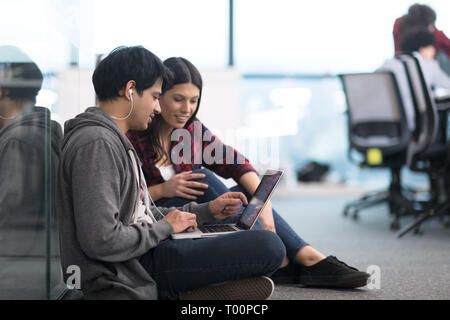 young software developers couple using laptop computer writing programming code while sitting on the floor at modern creative startup office Stock Photo