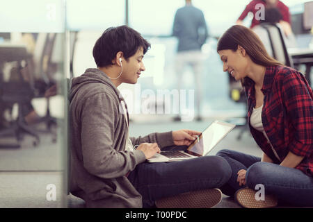 young software developers couple using laptop computer writing programming code while sitting on the floor at modern creative startup office Stock Photo