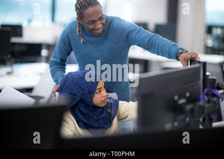 black muslim female software developer working together with her african american male colleague using computer while writing programming code at mode Stock Photo