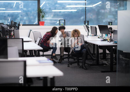 group of young female software developers using mobile phones writing messages while having a break at modern startup office Stock Photo