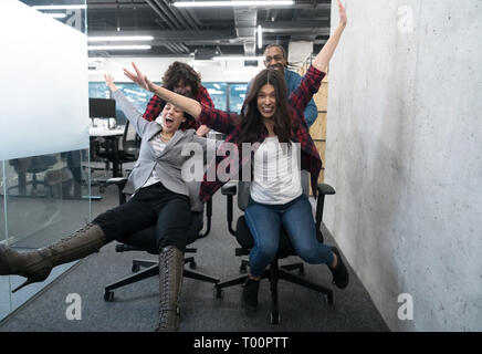 multiethnics startup business team of software developers having fun while racing on office chairs,excited diverse employees laughing enjoying funny a Stock Photo
