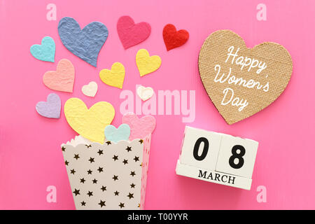 wooden March 8 calendar next to paper colorful hearts over pink wooden background Stock Photo