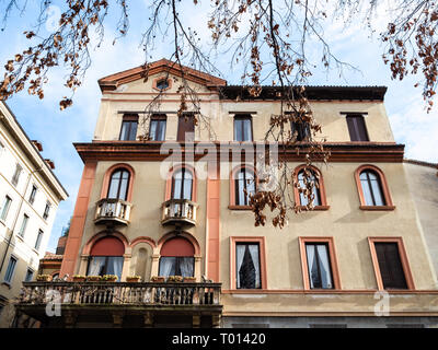 Travel to Italy - tree twig with dried autumn leaves and apartment house on street via Caradosso in Milan city in sunny day, Lombardy Stock Photo