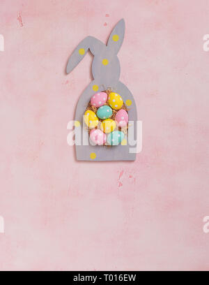 Colorful polka dot easter eggs in rabbit-shaped frame on pink concrete background, postcard concept Stock Photo