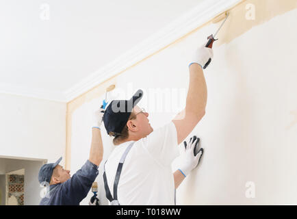 Two workers paint a wall in the room using rollers. Stock Photo