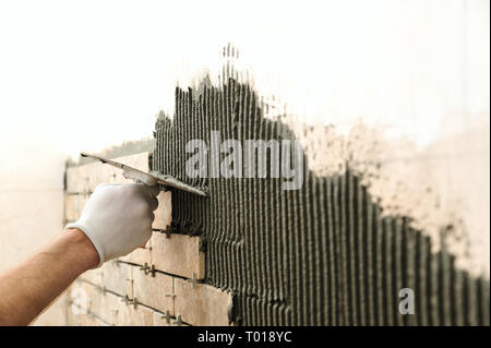 Installing the tiles on the wall. A worker setting tiles in the form of brick. He put adhesive using a comb trowel. Stock Photo