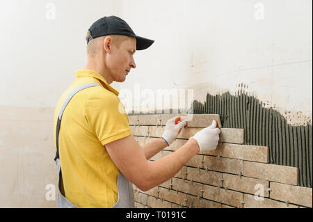 Installing the tiles on the wall. The worker putting tiles in the form of brick. Stock Photo