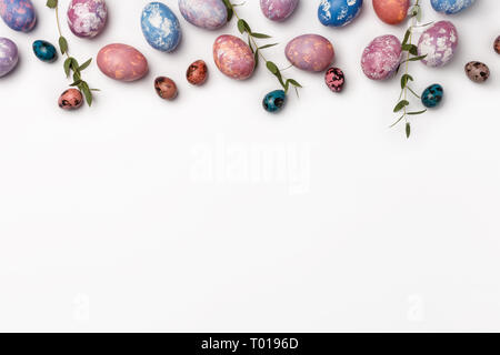 Top view of easter eggs colored with blue, pink, purple and orange paint in different patterns with green leafs of plant. Various abstract designs iso Stock Photo