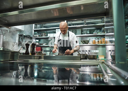 Professional chef. Famous young chef in black apron working at his modern restaurant kitchen. Cooking process Stock Photo