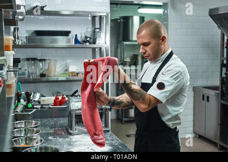 Italian food. Handsome professional chef holding a dough for homemade pasta while standing in restaurant kitchen. Cooking process Stock Photo