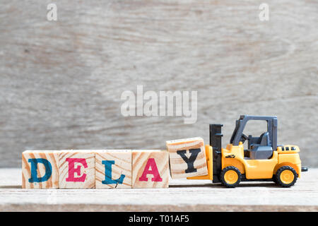 Toy forklift hold letter block y to complete word delay on wood background Stock Photo