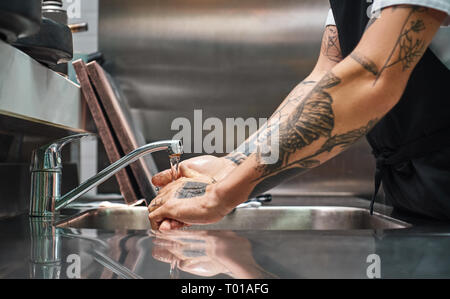 Before cooking...Close up photo of chef carefully washing his hands with different tattoos in a restaurant kitchen. Cropped view Stock Photo