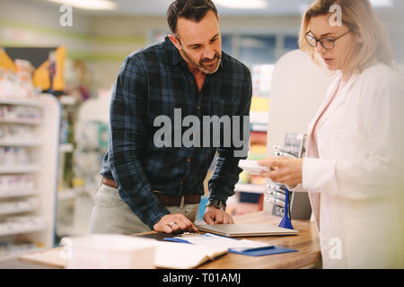 Female pharmacist showing medicine to male customer in pharmacy. Chemist suggesting medical drug to buyer in pharmacy drugstore. Stock Photo