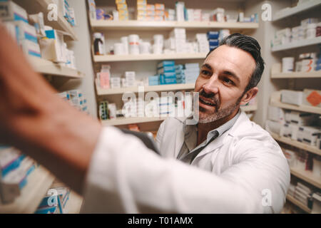 Professional pharmacist checking stock in an aisle of a local drugstore. Male chemist taking inventory at pharmacy store. Stock Photo