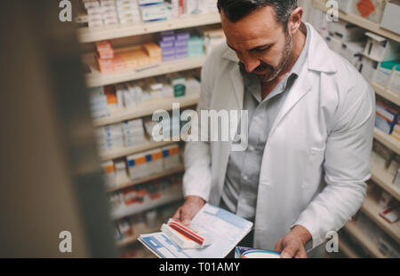 Male chemist looking for right medicine with a prescription in pharmacy. Pharmacist holding prescription and reading content on medicine box in pharma Stock Photo