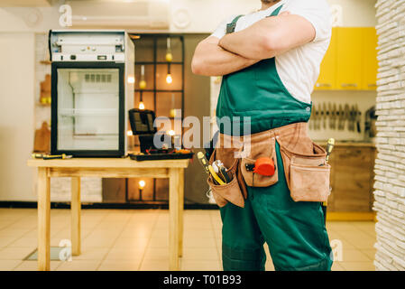Worker in uniform against refrigerator on table Stock Photo