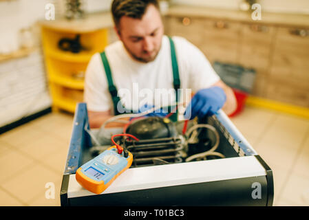 Worker in uniform testing refrigerator at home Stock Photo