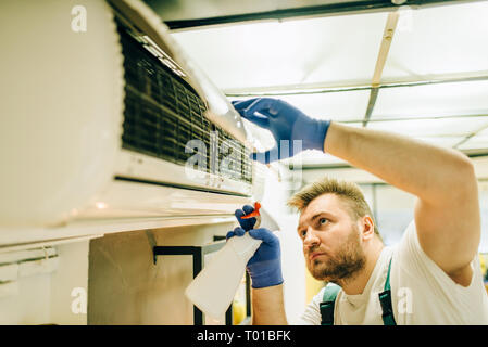 Repairman in uniform cleans the air conditioner Stock Photo
