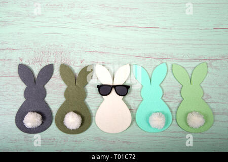Felt bunnies in earth tone colors in a row, middle bunny wearing fun sunglasses other bunnies bottoms forward. Hoppy Easter theme. Stock Photo