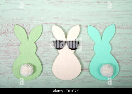 Felt bunnies in earth tone colors in a row, middle bunny wearing fun sunglasses other bunnies bottoms forward. Hoppy Easter theme. Stock Photo