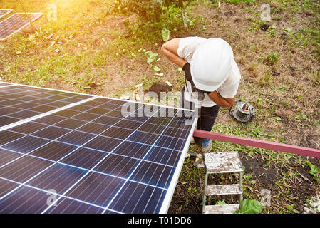 View from above of technician working with screwdriver connecting solar photo voltaic panel to exterior metal platform on sunny day. Alternative renew Stock Photo