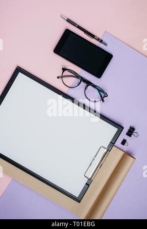 Creative flat lay, top view office table desk. Workspace with blank clip board, office supplies, pen, notepad, smartphone, eyeglasses on pink and viol Stock Photo