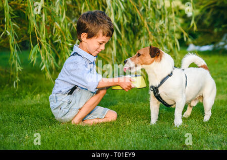 Small boy holding dog bowl in hands to water thirsty his pet dog Stock Photo