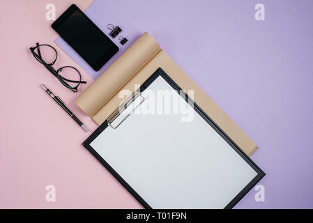 Flat lay, top view office table desk. Workspace with blank clip board, office supplies, pen, smartphone and glasses on pink and violet background. Blo Stock Photo