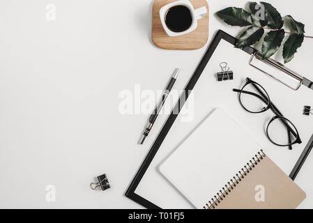 Home office workspace mockup with blank clip board, office supplies, pen, green leaf, coffee cup on a wooden stand and eyeglasses on white background. Stock Photo