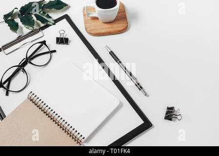 Home office workspace mockup with blank clip board, office supplies, pen, green leaf, coffee cup on a wooden stand and eyeglasses on white background. Stock Photo