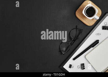Mock up workspace with blank clip board, office supplies, pen, coffee cup, notepad and eyeglasses on dark background. Flat lay, top view, copy space Stock Photo
