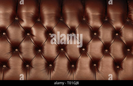 Background texture of dark brown capitone genuine leather, retro Chesterfield style soft tufted furniture upholstery with deep diamond pattern and but Stock Photo