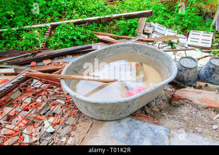 Concrete mixer plastic empty At have water on garbage timber pile in construction house renovate site and sunrise light Stock Photo