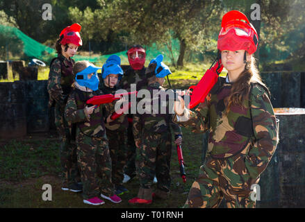 sportive cheerful girl paintball player in camouflage standing with gun before playing outdoors Stock Photo